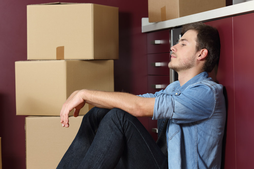 Dissatisfied tenant sitting against cabinet next to stacked boxes