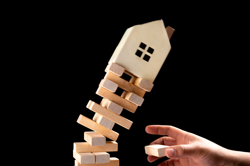 Jenga game falling with wooden house on top. Property management concept.