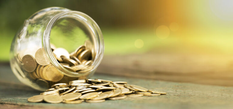 Coins in jar spilling out onto table.
