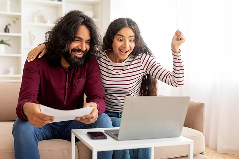 Indian couple happy watching a laptop and holding a paperwork