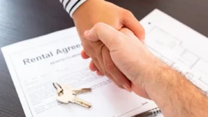 Hands shaking in the foreground with a rental agreement and keys featured in the background.