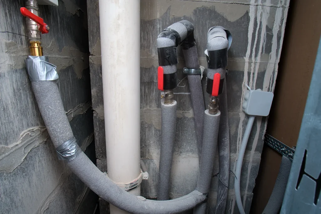 Plumbing pipes with grey insulation wrapped around them.