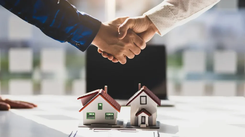 People shaking hands over two small model houses.