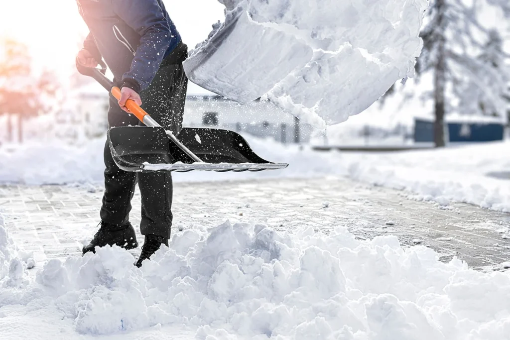 A person removing snow from a driveway with a snow shovel.