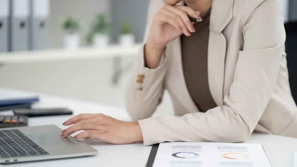 Real estate professoinal working at a laptop with paperwork on the desk.