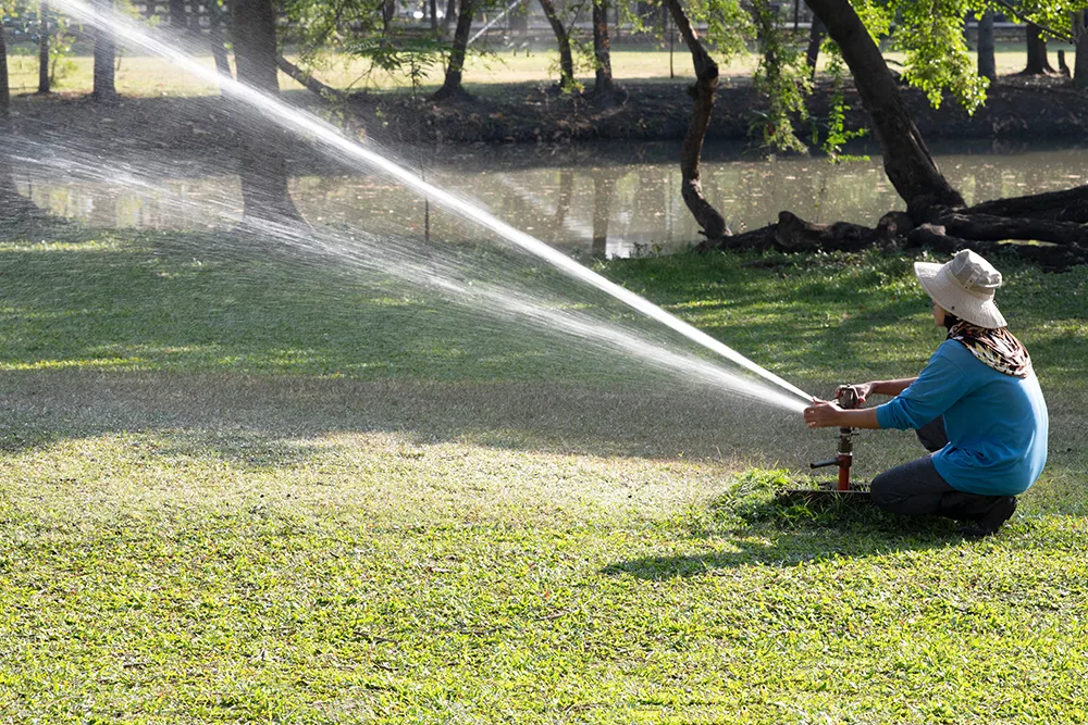 A person adjusting a tall sprinkler on a green lawn