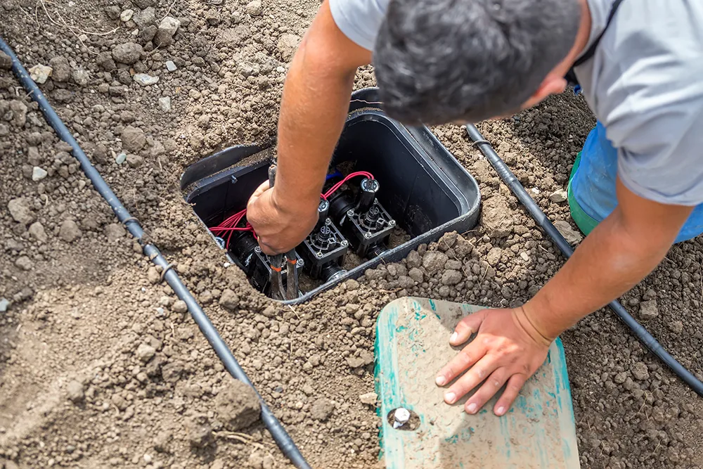 Pair of hands working providing Wasatch Front irrigation maintenance in a sprinkler box in the ground