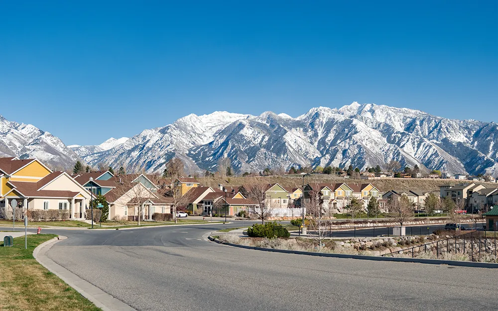 A road with a bend in the background that leads into a neighborhood in front of snowy mountains