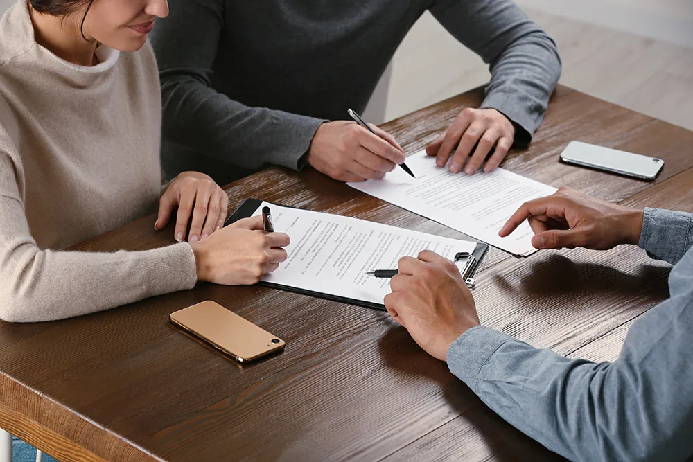 Two people pictured with a property manager going over paperwork on a desk.